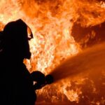 firefighter in the shadows putting out a massive fire with a fire hose