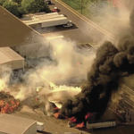 aerial shot of a facility up in smoke, with a huge fire